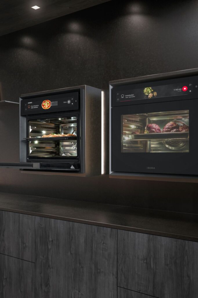 Two BORA XBO ovens side by side, filled with roasting trays of chicken and vegetables.