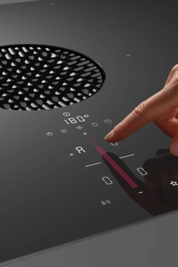 Hand adjusting power level on BORA S Pure induction cooktop with round air inlet and glowing icons.