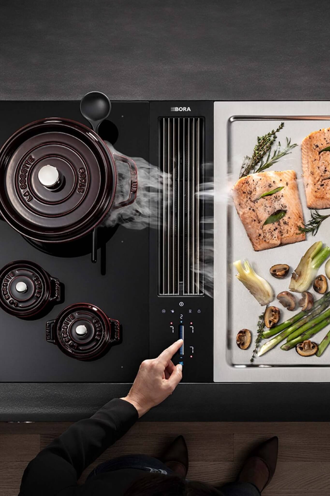 Overhead view of BORA Classic cooktop with pans, grilled asparagus, and modern downdraft extractor.