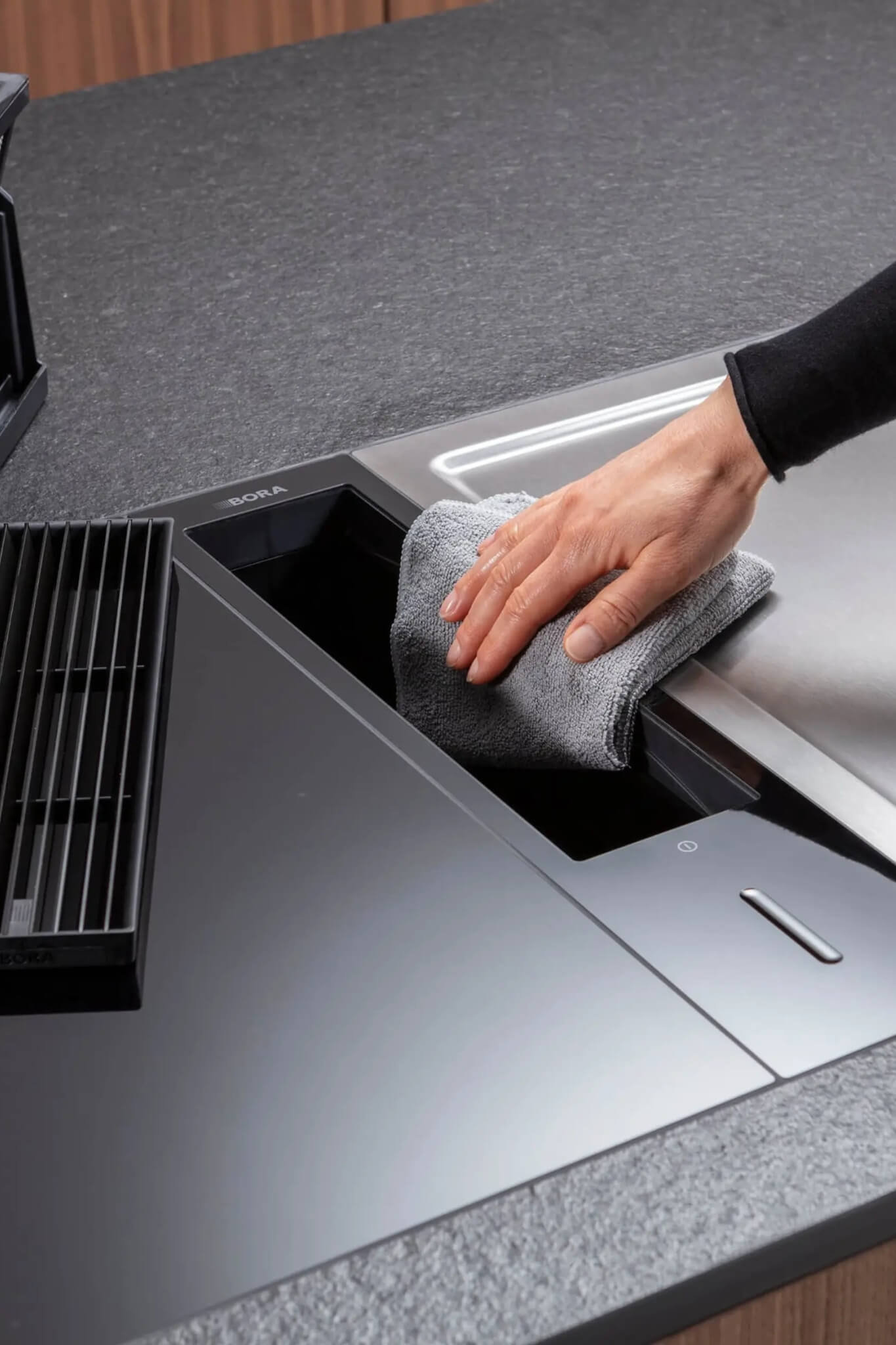 Hand cleaning stainless vent on BORA Classic cooktop set in grey countertop.