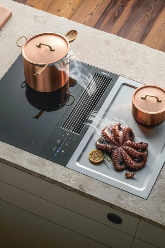 Copper pots cooking sausages on light stone surface with BORA Classic vent between zones.